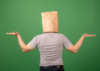 Unrecognizable man with a paper bag on his head on a green background. Choice, greenwashing, disinformation concept