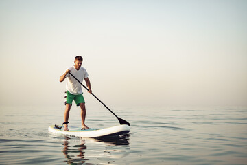 Fototapeta na wymiar Young man in t-shirt and shorts floating on SUP board
