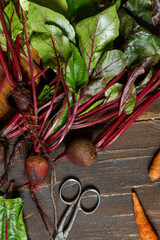 Raw beetroot with tops and carrots on a rough wooden table. Close-up, top view, vertical