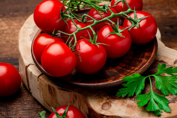 Branch of fresh cherry tomatoes with greens on a brown wooden background.