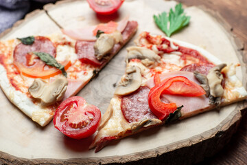 Pizza with ham and bacon, mushrooms and tomatoes on a slice of wood on a brown wooden background.