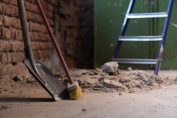 Shovel and broom on the dusty construction site floor background.
