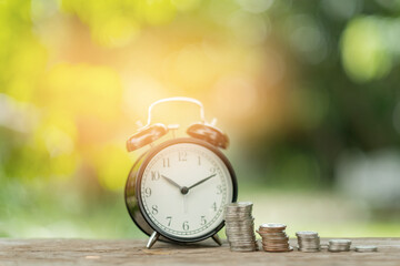 Alarm clock with step of coins on wood table with green nature background
