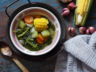 Sayur bening bayam or spinach clear soup is Indonesian food made from spinach, carrot, corn, and other vegetables. Served on white bowl on wooden table. Taste refreshing, easy to cook. Comfort food.