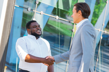 African-American businessman and his colleague in front of modern office building. Financial investors are talking outdoor. Banking and business concept.