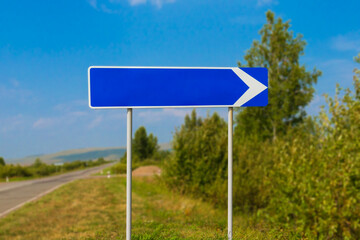 Blue empty signpost with white arrow on summer rural road. Mock up for our text. Blank direction sign. Background with copy space