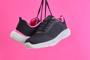 Pair female sports sneakers for run and fitness hanging by shoelaces on pink background. Fashion...