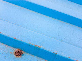 Diagonal lines on a blue rusty textured metal surface of a tin roof with an old rusted iron screw.