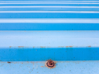 Geometric horizontal line patterns on the close up of a rusty blue tin roof.