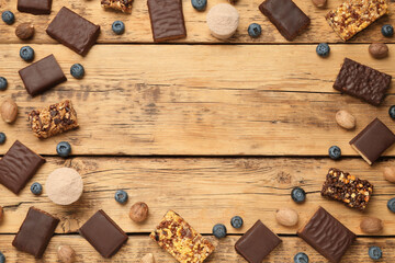 Frame of different energy bars, nuts, blueberries and protein powder on wooden table, flat lay. Space for text