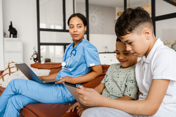 Black woman doctor and her sons using gadgets while sitting on couch