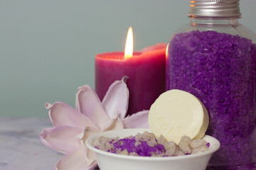 Fototapeta na wymiar A jar of purple lavender sea salt, bowl with a round bar of soap, burning lilac candle, beautiful flower composition. Spa treatment, body and facial care. Cosmetic products. Women's beauty. Copy space