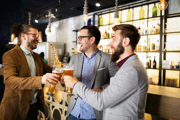 Happy young businessmen drinking beer and talking at pub after work