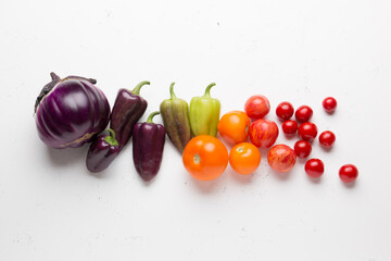 Radishes, tomatoes, cherry tomatoes, round eggplants, peppers, green tops on a light background. Mix of different vegetables on a white background.
