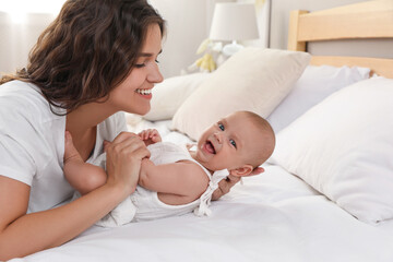 Happy young mother with her cute baby on bed at home