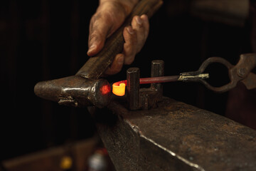 Close-up working powerful hands of male blacksmith forge an iron product in a blacksmith. Hammer, red hot metal and anvil. Concept of labor, retro professions