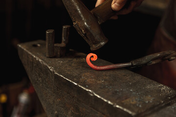 Close-up hands of male blacksmith forge an iron product in a blacksmith. Hammer, red hot metal and anvil. Concept of labor, retro professions