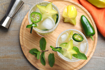 Glasses of spicy cocktail with jalapeno, carambola and mint on wooden table, flat lay