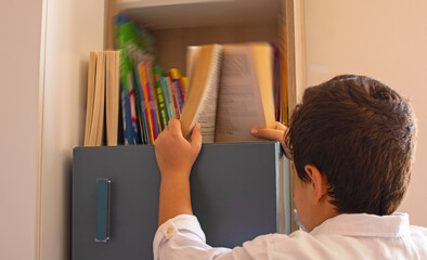 a boy taking a book to read from his library.