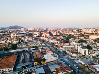 Imágem aérea da Avenida Dom Hélder Câmara com residências, industria e comércio com por do sol ao fundo na zona norte da cidade do Rio de Janeiro.