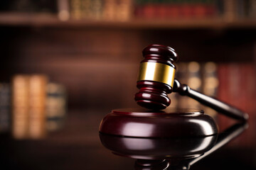 Law theme. Judge chamber. Gavel on brown desk. Collection of legal books in the bookshelf.