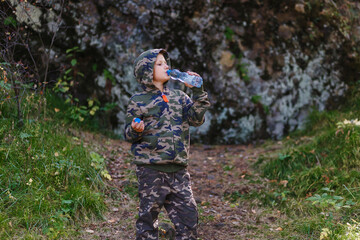 boy tourist in hoodie and hood drinks bottled water in the autumn in the mountains