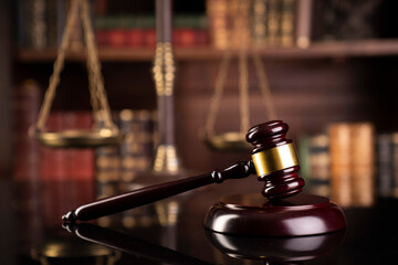 Law theme. Judge chamber. Gavel on brown desk. Collection of legal books in the bookshelf.