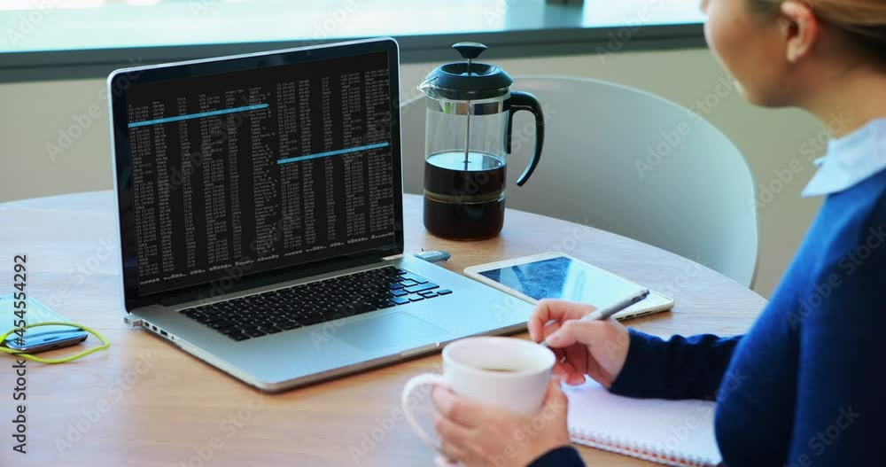 Poster caucasian woman sitting at table watching coding data processing on laptop screen and making notes