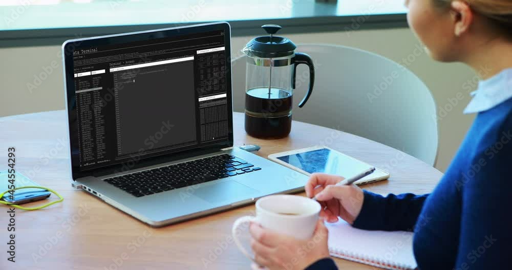 Poster caucasian woman sitting at table watching coding data processing on laptop screen and making notes