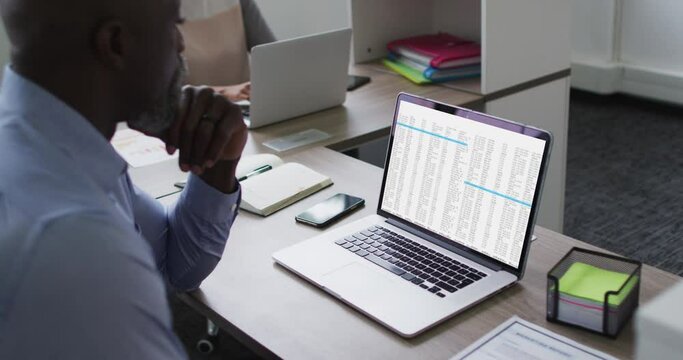 African american man sitting at desk watching coding data processing on laptop screen