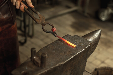 Close-up working powerful hands of male blacksmith forge an iron product in a blacksmith. Hammer,...