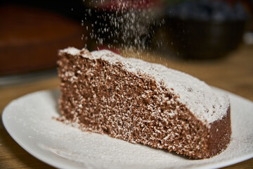 A woman with a passion for cooking decorates a slice of handmade chocolate cake in her home kitchen with blackberries, red currants and a sweet white rain of powdered sugar.