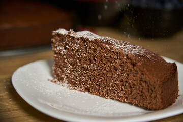 A woman with a passion for cooking decorates a slice of handmade chocolate cake in her home kitchen with blackberries, red currants and a sweet white rain of powdered sugar.