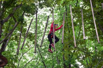 Teen boy crossing the suspension bridge in the rope summer park © Serhii