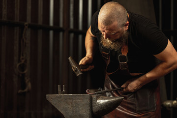 Bearded man, blacksmith working on creating handmade metal product at family smithy. Concept of labor, retro professions, power, beauty