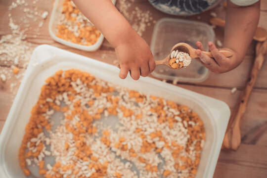 Baby Kid Playing Sensory Games To Develop Motor Skills With Dry Pasta And Peas, Wood Spoons.