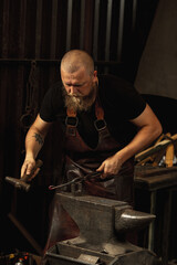 Bearded man, blacksmith manually forging the molten metal on the anvil in smithy with spark fireworks. Concept of labor, retro professions, family business