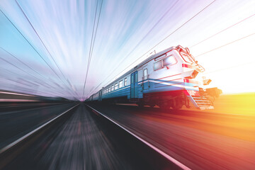 Fototapeta premium Old suburban train in motion against the background of sunrise - sunset. Ukrainian railway. Passenger train at speed
