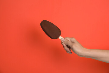 Woman holding ice cream glazed in chocolate on red background, closeup