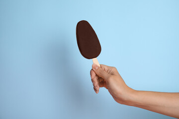 Woman holding ice cream glazed in chocolate on light blue background, closeup