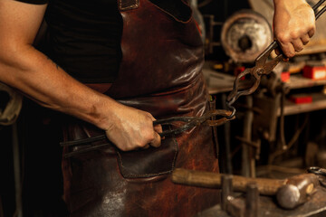 Close-up hands of male blacksmith forge an iron product in a blacksmith. Hammer, red hot metal and anvil. Concept of labor, retro professions