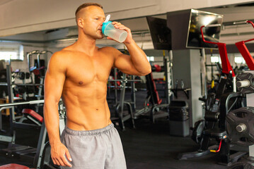 Obraz premium Young caucasian man drinking water after exercise.man in the gym drinking from the shaker.