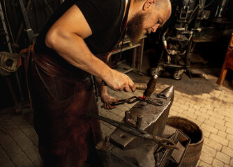 Bearded man, blacksmith working on creating handmade metal product at family smithy. Concept of...