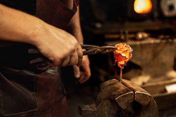 Beautiful rose. Blacksmith manually forging molten metal on anvil in smithy with spark fireworks....