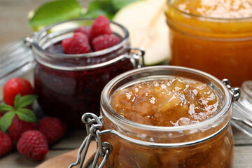 Jars with different jams and fresh berries on wooden table, closeup