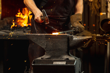 Bearded man, blacksmith manually forging the molten metal on the anvil in smithy with spark...