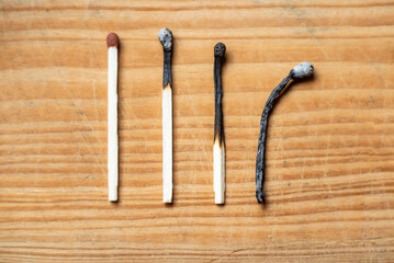 Row of burnt matches and whole one on wooden background, top view,closeup. Concept of different phases in human life.
