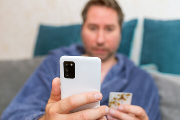 A man uses a mobile phone to pay for goods ordered in an online store. Concepts of using mobile technologies and smarfon in mobile applications at home.