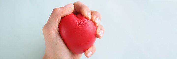 Female hand holding red toy heart on blue background closeup