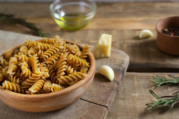 Raw fusilli in a wooden bowl on a cutting board with ingredients on a wooden table. Rustic style. Horizontal orientation. Italian food concept.
